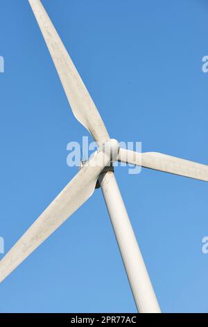 Primo piano di una turbina eolica e delle pale dell'elica su uno sfondo blu del cielo dal basso. Raccolta di una fonte di energia sostenibile e rinnovabile per generare energia ed elettricità da climi ventosi Foto Stock