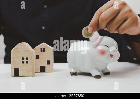 Mano che tiene la moneta di risparmio piggy banca finanza investimento prestito casa. Economia di affari concetto di proprietà immobiliare. Foto Stock