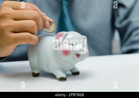 Uomo d'affari mano che detiene moneta risparmio di denaro piggybank sul tavolo.conto finanziario aziendale tassa di investimento economia assicurazione e piano pensione concetto. Foto Stock