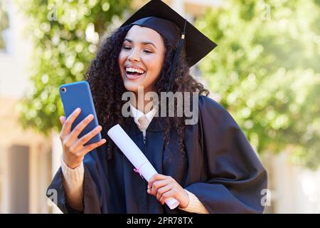 Devo dire a tutti i miei grandi successi. Scatto di una giovane donna usando un cellulare il giorno della laurea. Foto Stock