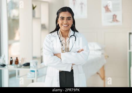 Vi fa sentire meglio. Un giovane medico attraente in piedi da solo nella sua clinica con le braccia piegate. Foto Stock