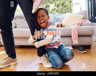 HES che ha una brutta giornata. Un ragazzino che lancia un tantrum mentre tiene la gamba dei genitori a casa. Foto Stock