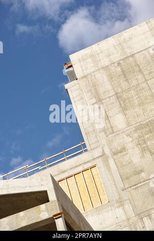 Esterno di un edificio in cemento contro un cielo blu nuvoloso. Vista dettagliata di un alto edificio residenziale o di uffici realizzato con lastre di cemento esposte. Fase di costruzione della ristrutturazione e aggiunta della casa Foto Stock