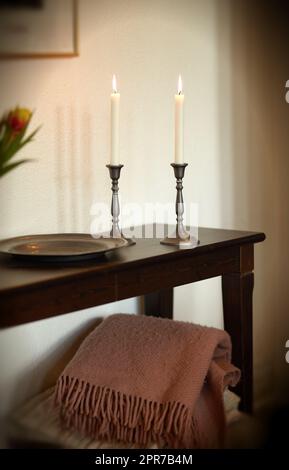 Candele luminose eleganti e decorative su un tavolo di legno a casa. Decorazioni in tessuto e casalinghi per un aroma, un buon profumo e per riscaldare una stanza. Arredamento accogliente per un appartamento moderno Foto Stock