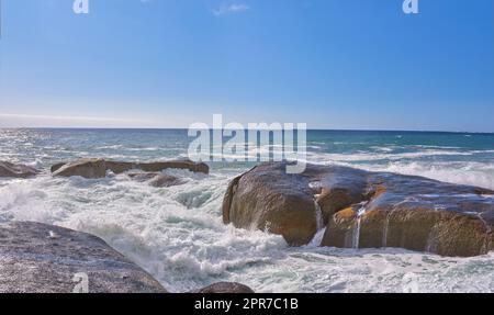 Vista panoramica delle onde oceaniche e del lavaggio d'acqua su massi e rocce a Camps Bay, città del Capo, Sudafrica. Paesaggio tropicale vuoto con cielo blu e spazio per copiare. Viaggi, turismo all'estero e all'estero Foto Stock