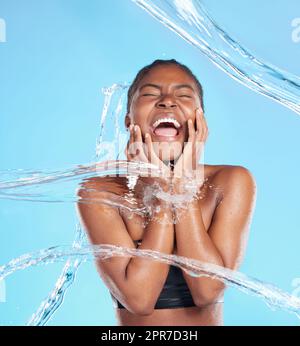 Sentitela bagnare. Scatto di una bella giovane donna che viene spruzzata con acqua su uno sfondo blu. Foto Stock