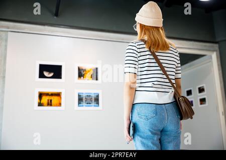 Donna asiatica che guarda una galleria d'arte di fronte a quadri colorati incorniciati Foto Stock