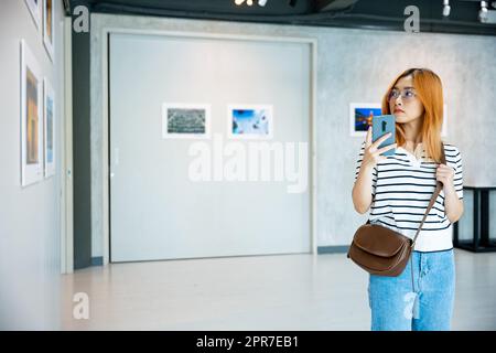 La donna visitatrice in piedi scatta foto della galleria d'arte davanti a quadri incorniciati Foto Stock