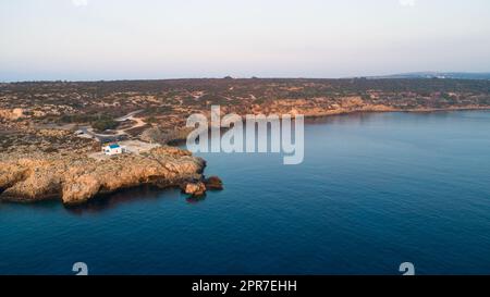 Vista aerea del tramonto della costa e simbolo bianco cappella Agioi Anargyroi, a cavo Greco Protaras, Famagosta, Cipro dall'alto. Vie dell'occhio dell'uccello Foto Stock