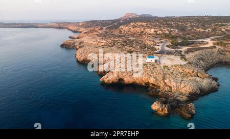 Vista aerea del tramonto della costa e simbolo bianco cappella Agioi Anargyroi, a cavo Greco Protaras, Famagosta, Cipro dall'alto. Vie dell'occhio dell'uccello Foto Stock