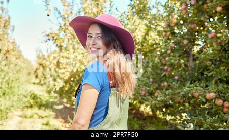 Ritratto di una bella lavoratrice agricola che si trovava in una fattoria durante la stagione del raccolto. Giovane agricoltore felice tra alberi da frutto in una giornata di sole d'estate. Industria agricola che produce prodotti freschi Foto Stock