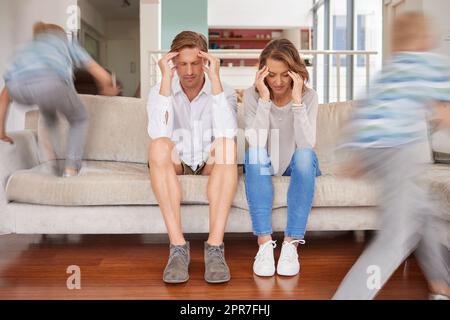 Bambini birichini iperattivi ed energici che infastidiscono la madre e il padre a casa. I genitori stanchi e stressati soffrono di mal di testa e affaticamento mentre i bambini adhd corrono in salotto essendo rumorosi. Foto Stock