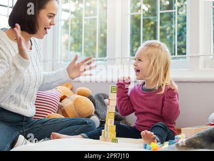 Un po 'di allegria su può arrivare lontano. Una bambina impilare blocchi con sua madre a casa. Foto Stock