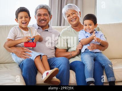 Ritratto di nonni sorridenti mentre tenevano i nipoti su un divano nel salotto. Uomo e donna ispanici anziani che trascorrono del tempo con i loro nipoti nel salotto di casa Foto Stock