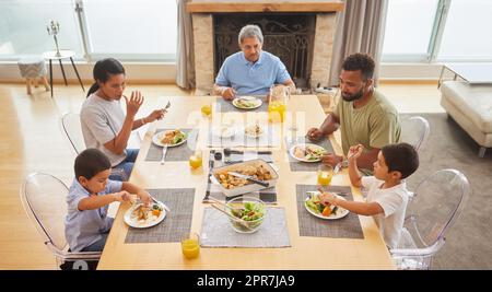 Vista dall'alto di una famiglia di corse miste seduto a un tavolo per pranzare nella sala di casa. I nonni ispanici mangiano con i loro figli e nipoti a casa Foto Stock