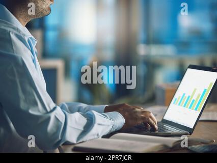 Closeup giovane africano che lavora su un portatile. Uomo d'affari afroamericano che usa un computer mentre lavora a tarda notte nel suo ufficio. Fare straordinari al di fuori dell'orario di lavoro per garantire successo e crescita Foto Stock