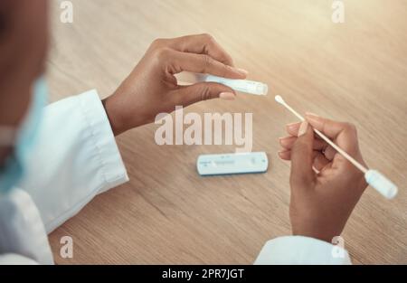 Mani di un medico in possesso di un test covid e di un campione di tampone. Primo piano sulle mani del medico afroamericano utilizzando un test del virus corona. gp dedicato che detiene il campione di test covid nella clinica Foto Stock