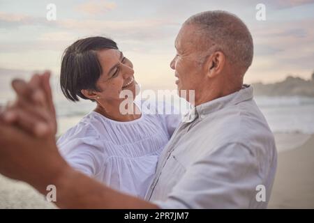 Affettuosa coppia matura mista che condivide un momento intimo e balla sulla spiaggia. Marito e moglie anziani al mare. Amano trascorrere del tempo insieme sulla costa in estate al tramonto Foto Stock