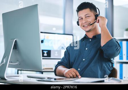 Ritratto di un agente di telemarketing ispanico felice che parla con una cuffia mentre lavora su un computer in ufficio. Consulente maschio sicuro e amichevole che gestisce un helpdesk per l'assistenza clienti e il supporto alle vendite Foto Stock