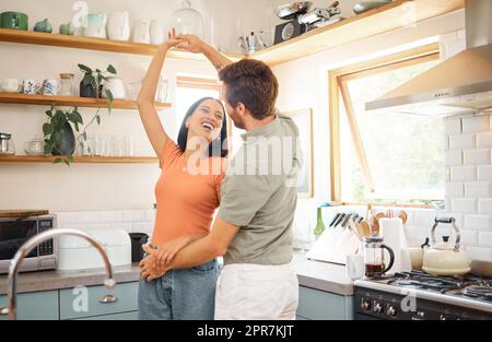 Giovani contenuti interrazziali coppia ballare in cucina a casa. Giocoso ragazzo caucasico e fidanzata di razza mista che si divertono. Marito e moglie felici si rilassano e passano del tempo insieme la mattina Foto Stock