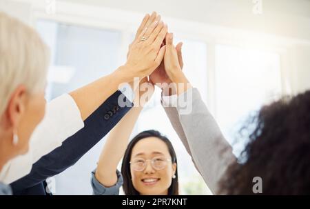 Gruppo di imprenditori diversi che si danno cinque in alto mentre si trovano insieme in un huddle in un ufficio. Colleghi ambiziosi che rimangono motivati e ispirati. Personale che celebra il successo e il successo come team unito Foto Stock