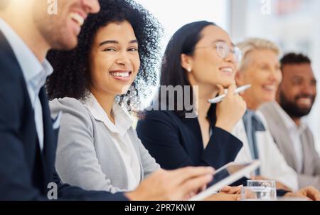 Ritratto di una giovane donna d'affari di razza mista che ascolta la presentazione durante la riunione nella sala riunioni dell'ufficio con diversi colleghi. Gli uomini d'affari sorridenti seduti in fila su un gruppo di persone che si sentono ispirati e motivati durante la conferenza Foto Stock
