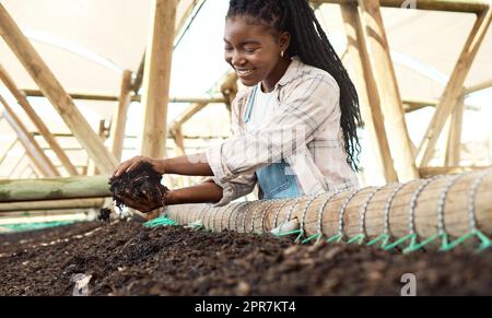 Contadino che tiene la terra con i vermi. Contadino felice che guarda il terreno con i vermi. Lavoratrice felice che controlla il suo terreno. Contadino afroamericano in un vivaio. Contadino che tiene un mucchio di terra. Foto Stock