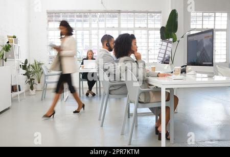 Gruppo di diversi operatori di call center che lavorano insieme in un ufficio occupato. Gli uomini d'affari rispondono alle chiamate mentre lavorano su un computer desktop a una scrivania in un ufficio. Operatori del servizio clienti che indossano cuffie o auricolari sul luogo di lavoro Foto Stock