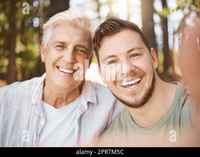 Incollaggio. Ritratto corto di un bel giovane uomo e suo padre che prende selfie mentre si accampano nei boschi. Foto Stock