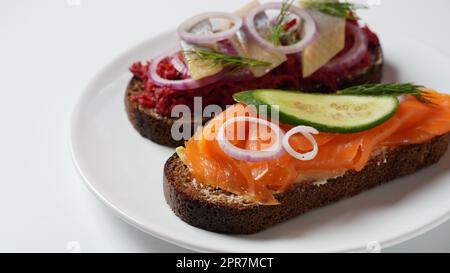 Panino Danese aperto Smorrebrod su pane di segale scuro con aringhe, salmone, barbabietole, cipolle rosse e ravanello Foto Stock