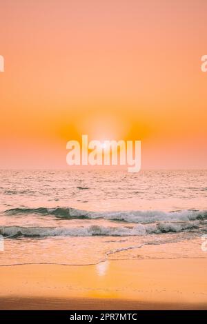 Tramonto sole splendere sopra il mare. Cielo naturale Alba colori caldi sul Mare di Ripple. Acqua di mare spruzzi di schiuma di lavaggio Sandy Beach Foto Stock