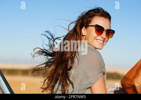 Il suo stile di vita è reale come lo è la strada aperta. Ritratto di bella giovane donna sorridente indossando corno occhiali da sole riammed. Foto Stock