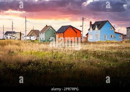 Terranova colorate case rustiche con pali di potenza che si affaccia su un campo erboso sotto un suggestivo tramonto cielo in Bonavista Canada. Foto Stock