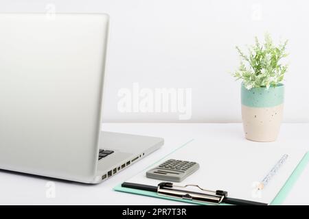 Lap Top, Appunti vuoti con carta, matita, Calcolatrice e vaso in ufficio. Scrivania con computer, notebook vuoto e Flower. Cancelleria sul posto di lavoro. Foto Stock