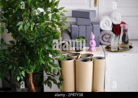 Una serie di attrezzature sportive nella sala yoga. Tappetini arrotolati per yoga, meditazione o fitness, blocchi e asciugamani. Foto Stock