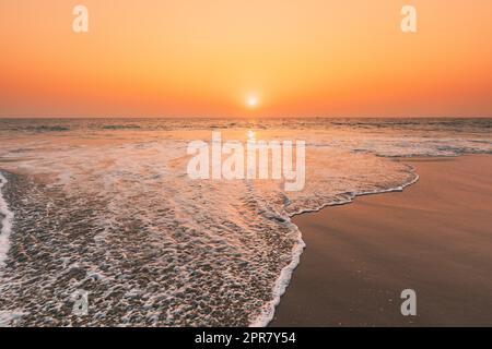 Tramonto Sole sopra Mare. Cielo naturale Alba colori caldi sul Mare di Ripple. Schiuma di acqua oceanica Lavaggio Sandy Beach al tramonto Foto Stock