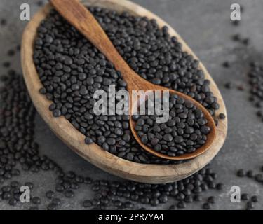 Ciotola di lenticchie nere secche con un cucchiaio su tavola grigia, fonte proteica per la dieta vegetariana Foto Stock