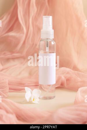 Un flacone dispenser con pompa vicino a fiori di orchidea bianchi e tulle rosa chiaro. Mockup Foto Stock