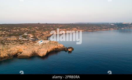 Vista aerea del tramonto della costa e simbolo bianco cappella Agioi Anargyroi, a cavo Greco Protaras, Famagosta, Cipro dall'alto. Vie dell'occhio dell'uccello Foto Stock