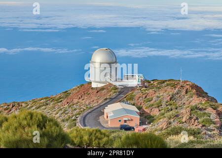 Osservatorio Roque de los Muchachos a la Palma. Una strada per un osservatorio astronomico con cielo blu e spazio copia. Telescopio circondato dal verde e situato su un'isola ai margini di una scogliera. Foto Stock