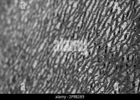 Primo piano monocromatico di un vetro di sicurezza laminato incrinato con messa a fuoco sul lato destro e sfocatura sbiadita sul lato sinistro, creando una texture astratta. Foto Stock