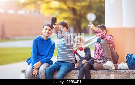 Bambini con zaini e cuffie seduti sulla panca del parco vicino alla scuola Foto Stock