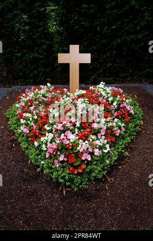 colorato cuore a forma di fiori disposti su una tomba con croce di legno Foto Stock