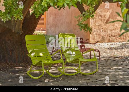 Due sedie a dondolo verdi d'epoca sotto un albero ombreggiato in un giardino appartato e privato di casa. Arredi da patio e posti a sedere per godersi e rilassarsi in estate. Rilassatevi e vi sentirete intimi all'esterno Foto Stock