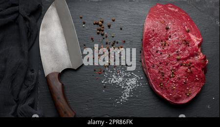 Filetto di manzo crudo giace su una tavola, tavolo nero. Foto Stock