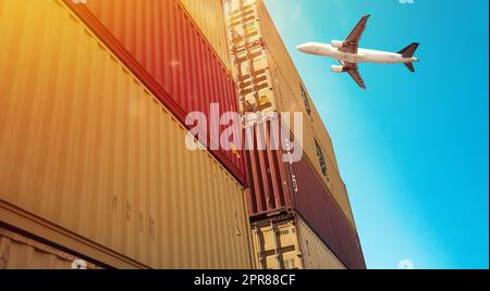 L'aeroplano vola sopra i contenitori accatastati nel porto Foto Stock