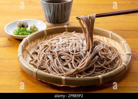 Zaru-soba e condimenti su un tavolo di legno. Prendi spaghetti di soba con le bacchette. Foto Stock