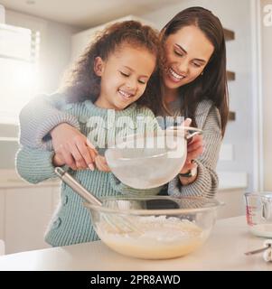 Questo è il segreto di una torta leggera e soffice. Shot di una mamma che cuoce con la figlia nella loro cucina a casa. Foto Stock