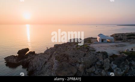 Vista aerea del tramonto della costa e simbolo bianco cappella Agioi Anargyroi, a cavo Greco Protaras, Famagosta, Cipro dall'alto. Vie dell'occhio dell'uccello Foto Stock