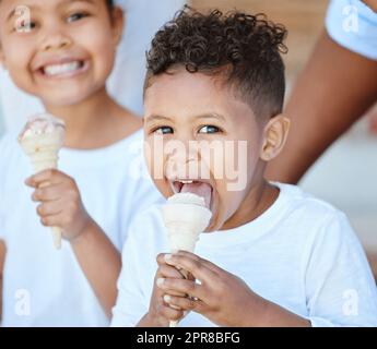 Dolce per i bambini. Shot di un adorabile ragazzo e ragazza che mangiano un cono gelato mentre si siede all'esterno. Foto Stock